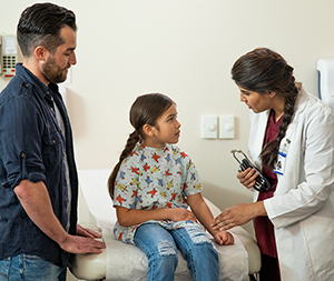 Un proveedor de atención médica hablando con un hombre y una niña en la sala de examinación.