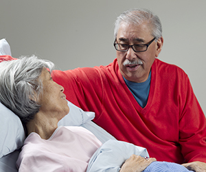 Woman lying in bed. Man sitting next to bed.