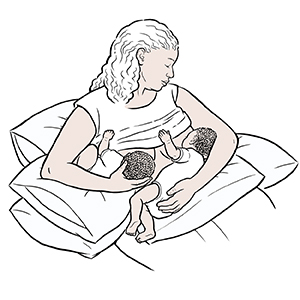 Woman breastfeeding twins with combination football and cradle holds.